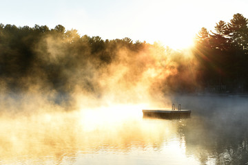 A gentle morning on the lake with fog over the water in the sun. USA. Maine