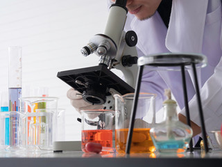 Scientist is looking at the microscope in the laboratory with white background and equipments.