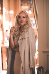 Stylish young girl 20-24 year old wearing beige elegant dress and autumn jacket posing in cafe closeup. Looking at camera.