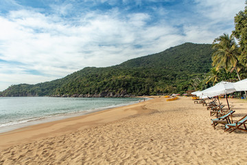 Beautiful panoramic view of Jabaquara beach in Ilhabela with chairs and umbrella on tropical island on the Brazilian sea coast during a sunny day of vacation and sightseeing trip.