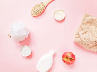 Flat lay feminine background. White sponge, face cream, sea salt, shampoo bottle, wooden comb, beige towel and fresh apple on a light pink. Mockup