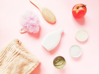 Beige cotton towel, sponge, shampoo bottle, wooden comb, blue clay mask, sea salt, face cream and apple on a pink background. Flat lay beauty photo