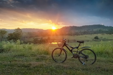 Fototapeta na wymiar Mountain view even Silhouette a bicycle parking on grass field around with forest, mountain and cloudy sky background, sunset at Thung Salang Luang National Park, Phetchabun, Thailand.