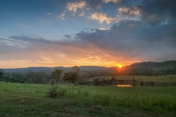 Mountain view evening of green grass field around with the hill with red sun light and cloudy sky background, sunset at Thung Salang Luang, Khao Kho, Phetchabun, Thailand.