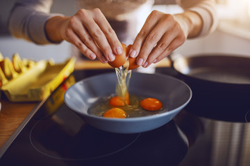 Close up of caucasian woman breaking egg and making sunny side up eggs. Domestic kitchen interior. Breakfast preparation. - obrazy, fototapety, plakaty