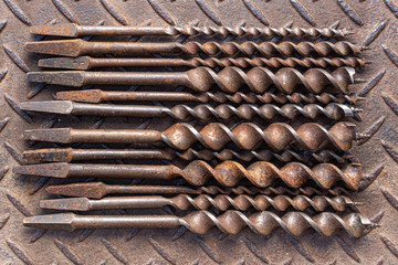 Vintage Brace Drill Bits arranged on rusted checker plate background.