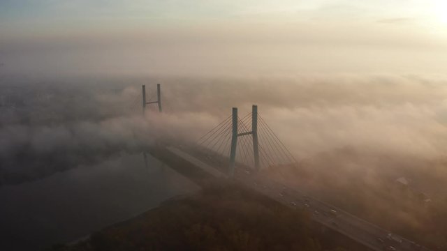 Aerial view of morning traffic over a bridge Siekierkowski, with dense fog at sunrise. Warsaw. Poland. Drone flies along a low fog bridge at sunrise.