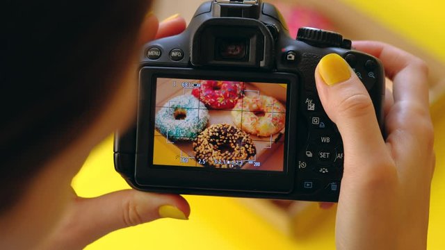 Close up - Food photographer take pictures with dslr camera of colored fresh donuts in box on yellow background. 4k. Concept of food photo blogging.