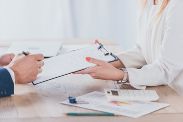 cropped view of businesswoman holding clipboard and man signing agreement