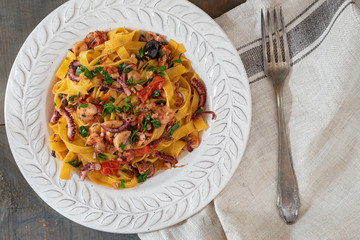 A plate of fettuccine with octopus, cherry tomatoes and black olives sauce.