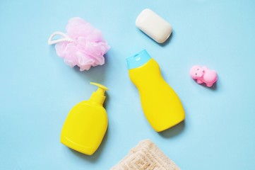 Yellow liquid soap, shampoo bottle, pink sponge on a blue background. Flat lay baby cosmetics set