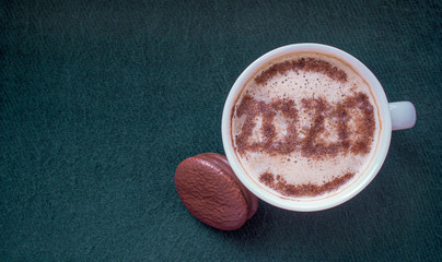 Mug of cappuccino with cinnamon on a dark cyanic background.Cinnamon powder was sprinkled with 2020 figures on coffee foam.Symbol of New year in a cup on coffee foam on woolen fabric.
