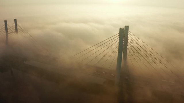 Aerial view of the fog passing through the Siekierkowski, Bridge. Warsaw. Aerial of the towers of the bridge with the movement of vehicles and a yacht passing along the river hung on a foggy morning.