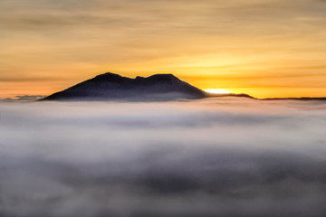 Mountain view misty morning of Peak Mountain around with ocean of mist with red and yellow sun light in cloudy sky background, sunrise at Thung Salang Luang, Khao Kho, Phetchabun, Thailand.