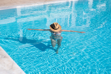 woman walking in a swimming pool with hat covering her face