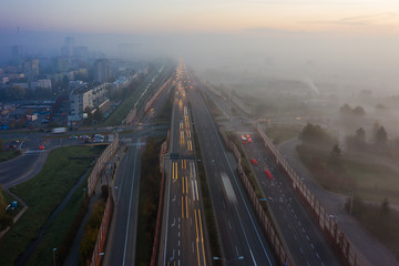 Fototapeta na wymiar Drone shot of a highway in Warsaw in the morning rush hour, with fog at dusk. Transport. Poland. Aerial view of a freeway with bridges and junctions at sunrise and fog. 