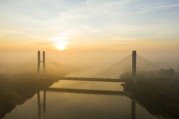 Aerial view of a bridge with cars in the fog. Warsaw. Poland. Drone shot at the traffic of a vehicle traveling in traffic jam on a bridge over a river. Drone shot into the fog at sunrise over a bridg