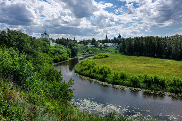 Fototapeta na wymiar Russia, Vladimir Oblast, Golden Ring, Suzdal: Panorama view with river Kamenka, green riverside and famous old orthodox churches, monasteries, convents in one of the oldest Russian towns, blue sky.