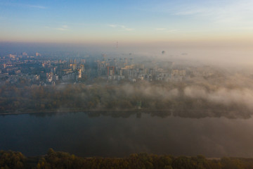 Fototapeta premium Drone flies towards the urban landscape with buildings in the fog at sunrise. Aerial view of cityscape in the fog at sunrise. Warsaw Poland.
