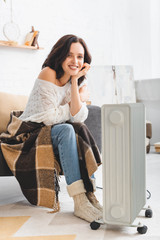 beautiful smiling girl with blanket warming up with heater in cold room