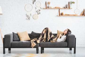 happy beautiful girl in blanket lying on sofa with laptop in cozy living room