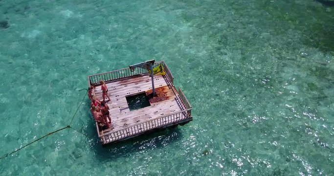 Aerial drone footage circling a wooden platform with a group of females above it in a crystal clear beach in Thailand 4K