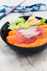 Japanese Chirashi made with assortment of three raw fishes, salmon, tuna and cod fish served on white vinegary rice with Wasabi sauce and ginger slices on top in a bowl.
