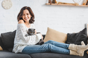 Obraz na płótnie Canvas beautiful happy girl sitting on sofa with scottish fold cat