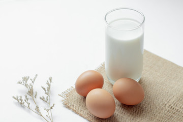 Glass of milk and eggs on white table and white background.