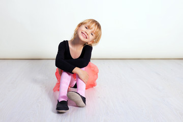 Little dancer girl in a pink tutu. Preschool kid sitting on hardwood floor. Cute child dancing...