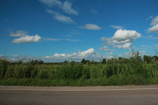 Take a photo of the meadow and the sky from the car parked on the road. beautiful sky and clouds in afternoon.