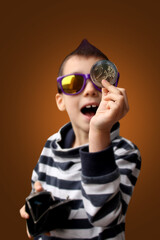 boy with a mohawk on his head, in dark sunglasses enthusiastically shows a large metal coin of 2 euros, business concept, close-up