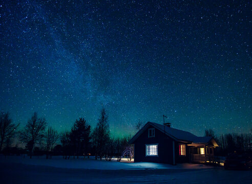 Cottage against the night sky with the Milky Way and the arctic Northern lights Aurora Borealis in snow winter Finland