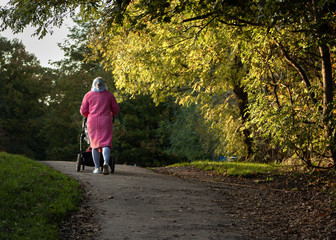 Despite the autumn sunshine a woman wraps up warm in a pink coat when taking a child in a pushchair...