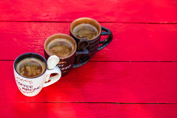Three cups of homemade expresso coffee on red wooden board.