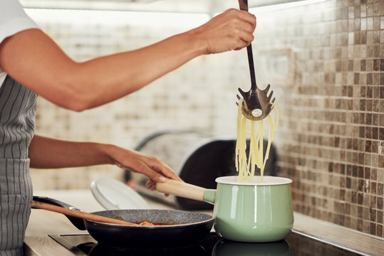 Cropped picture of mixed race woman in apron standing next to stove and making spaghetti.