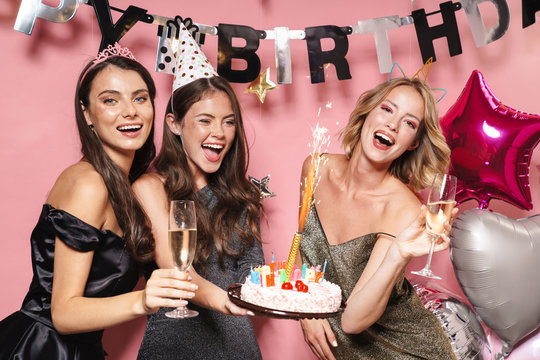 Image of joyful party girls holding birthday cake and champagne glasses