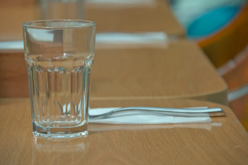 glass on top of wooden table with blurry restaurant . Empty glass on the wooden table in cafe. close up .