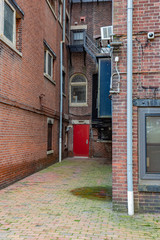 Rear entrance to old brick apartment buildings with red door, fire escape, vertical aspect