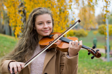 Girl playing the violin in the autumn park at a yellow foliage background. © allai