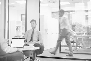 Attractive young businessman having job interview whilst people work in an active office in the background, job hunting concept