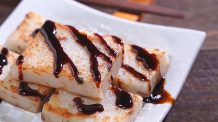 Pouring black soy sauce on ready-to-eat delicious turnip cake, Chinese traditional local dish radish cake in restaurant, close up, copy space.