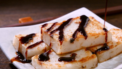 Pouring black soy sauce on ready-to-eat delicious turnip cake, Chinese traditional local dish radish cake in restaurant, close up, copy space.