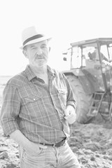 Fototapeta na wymiar Black and white photo of senior farmer standing against tractor in field
