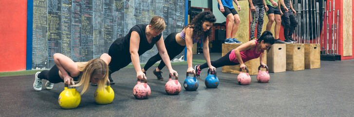 Sportswomen doing push-ups with kettlebells and sportsmen doing box jumps - Powered by Adobe