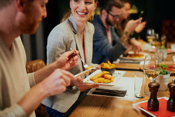 Handsome caucasian ginger taking food out of his girlfriend's plate while sitting in restaurant for...