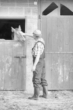Black and white photo of farmer petting horse in barn