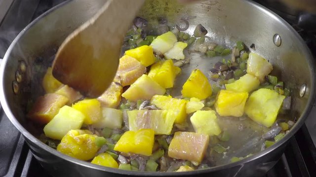 Normal Speed Followed By Slow Motion: Close POV Overhead Shot Of A Hand Stirring Chunks Of Mixed Raw Fish (cod, Smoked Haddock And Pink Salmon) With Vegetables, With A Wooden Spatula In A Frying Pan.