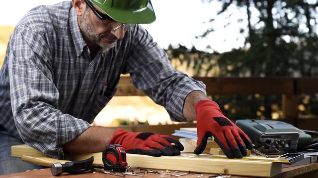 Adult carpenter craftsman wearing helmet and protective gloves, with a pencil and the carpenter's square trace the cutting line on a wooden table. Construction industry, housework do it yourself. Foot