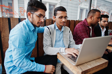 Group of four indian teen male students. Classmates spend time together and work at laptops.